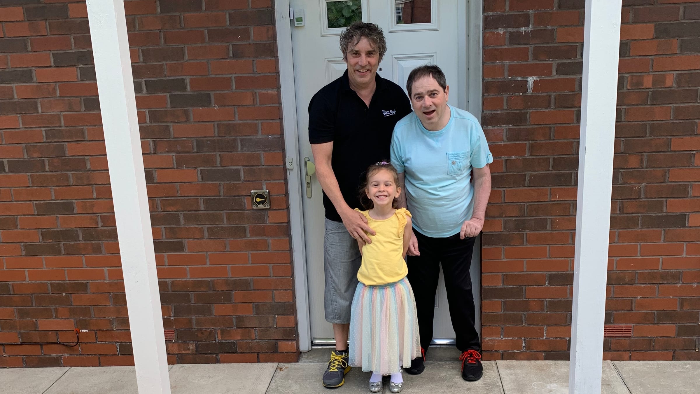 Alan Mountford-Brown standing in a doorway with his brother Gary and a young child, all smiling at the camera