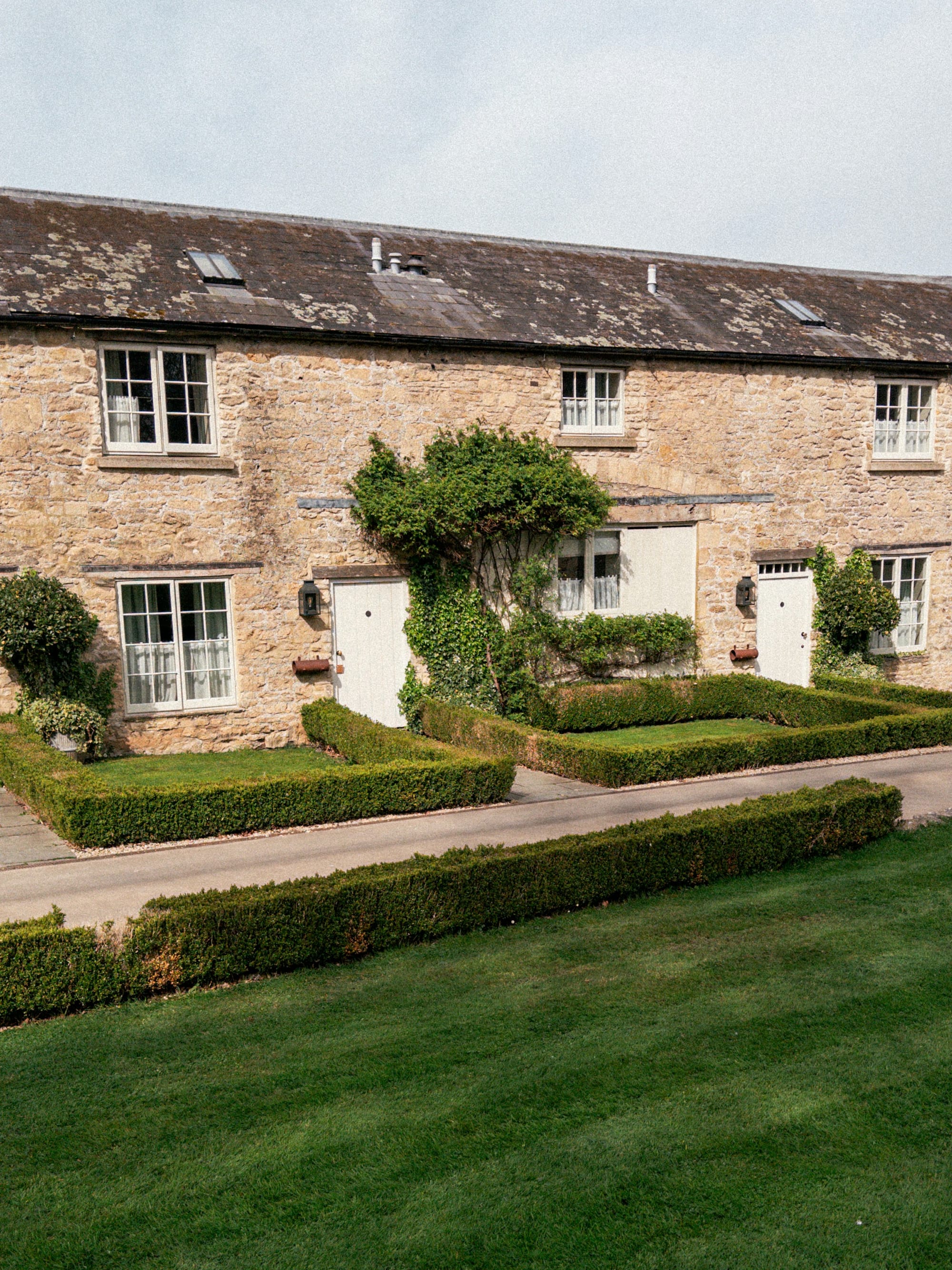 A stone farmhouse in the English countryside behind clipped hedges